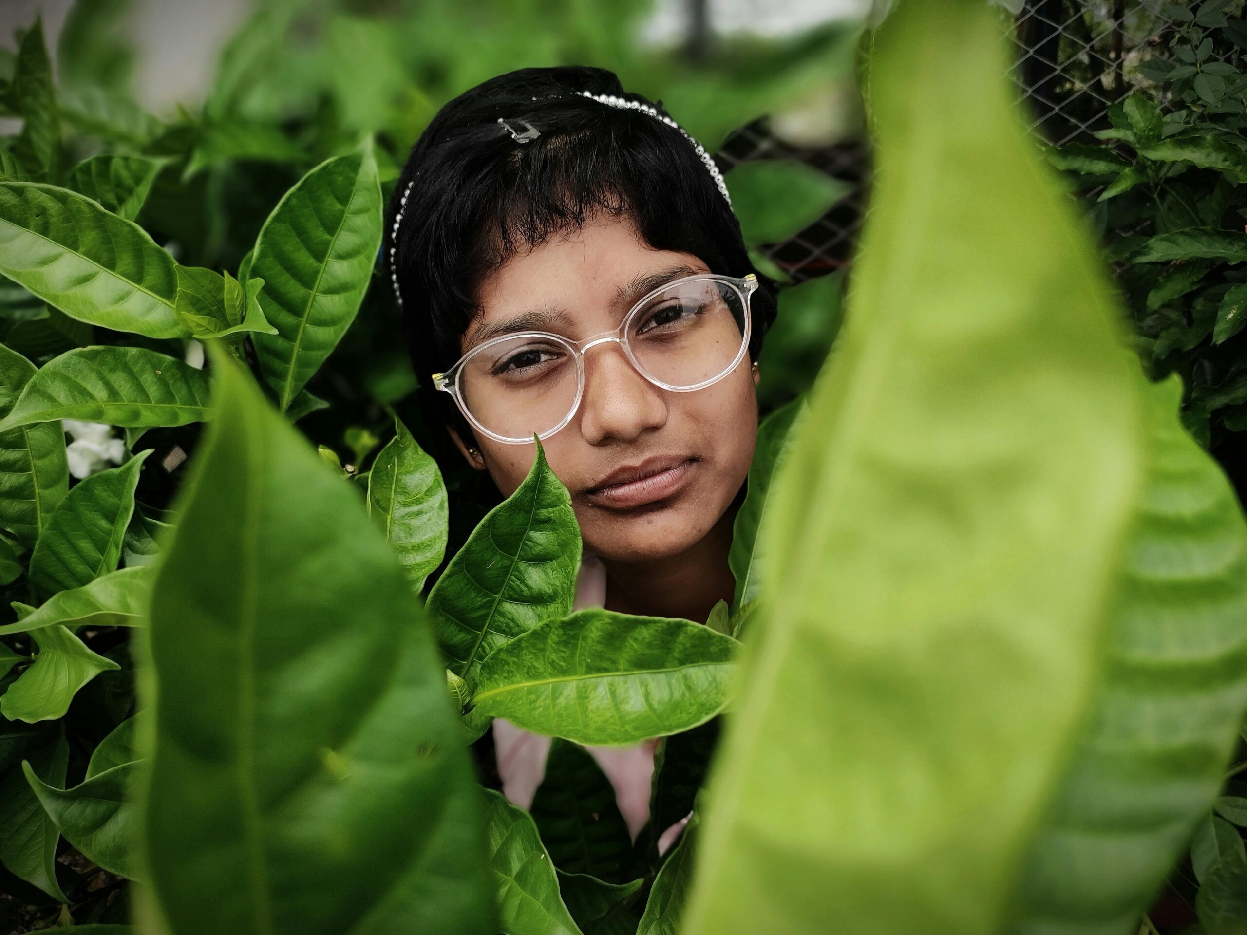 Close-up portrait of a woman partially hidden by lush green leaves outdoors.